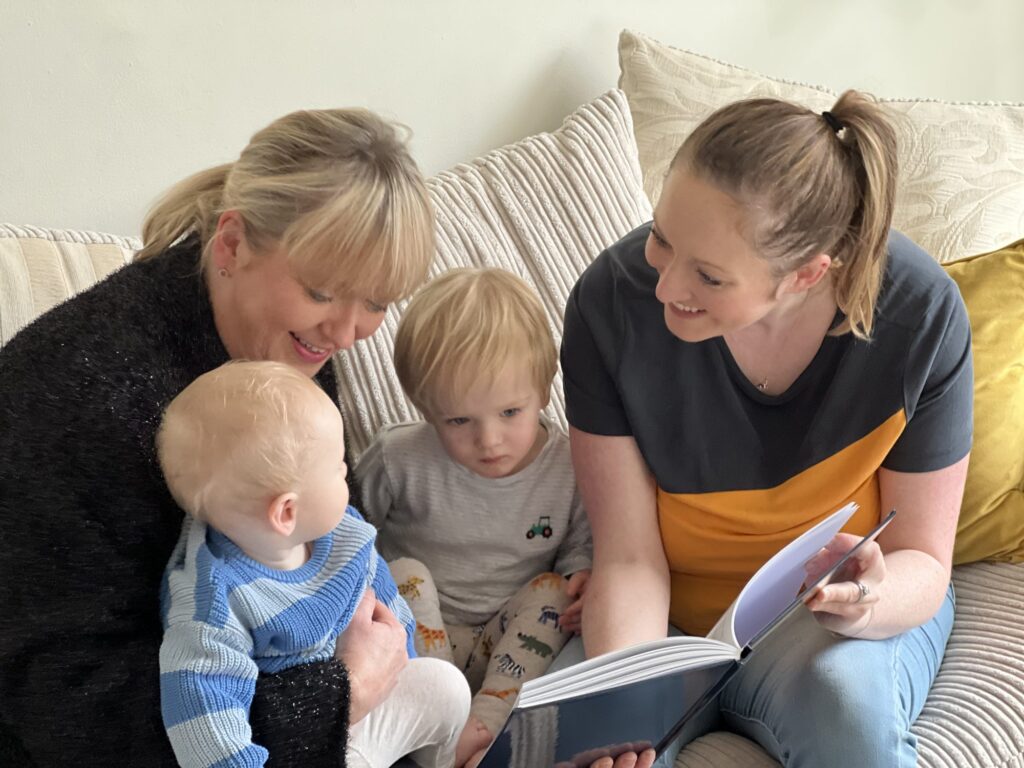 A grandmother, mother and two young children reading a YourStory book together on the sofa